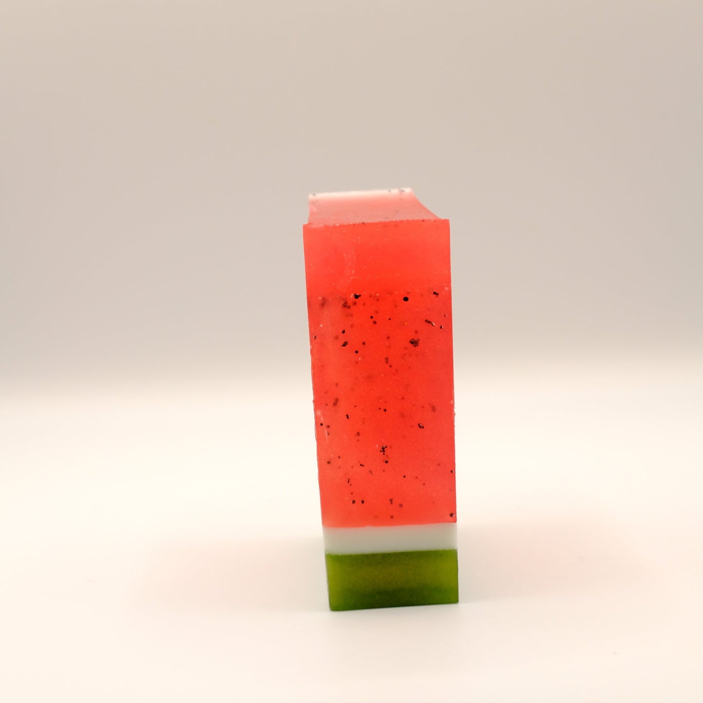 Side view of a bar of soap, bar has red at the top and green at the bottom on a light background