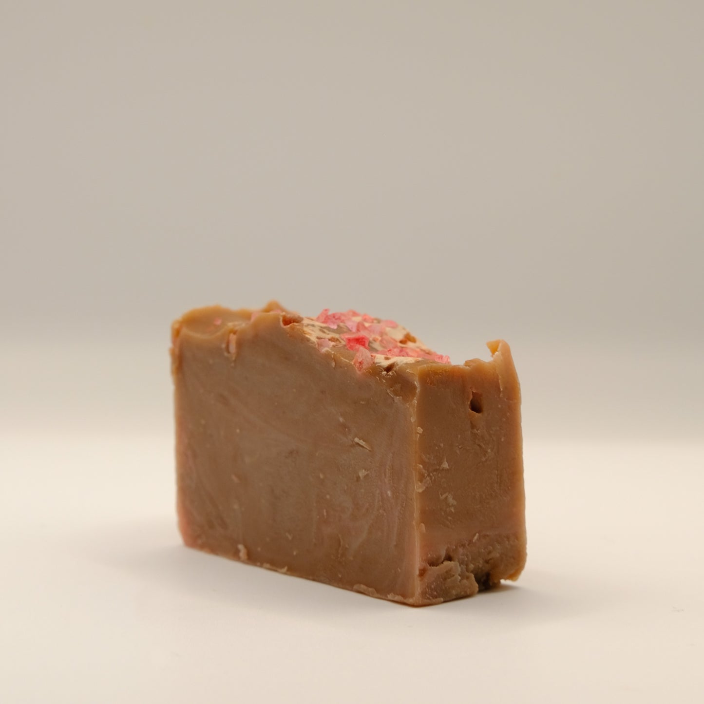 Bar of brown soap with pink speckles on a beige background