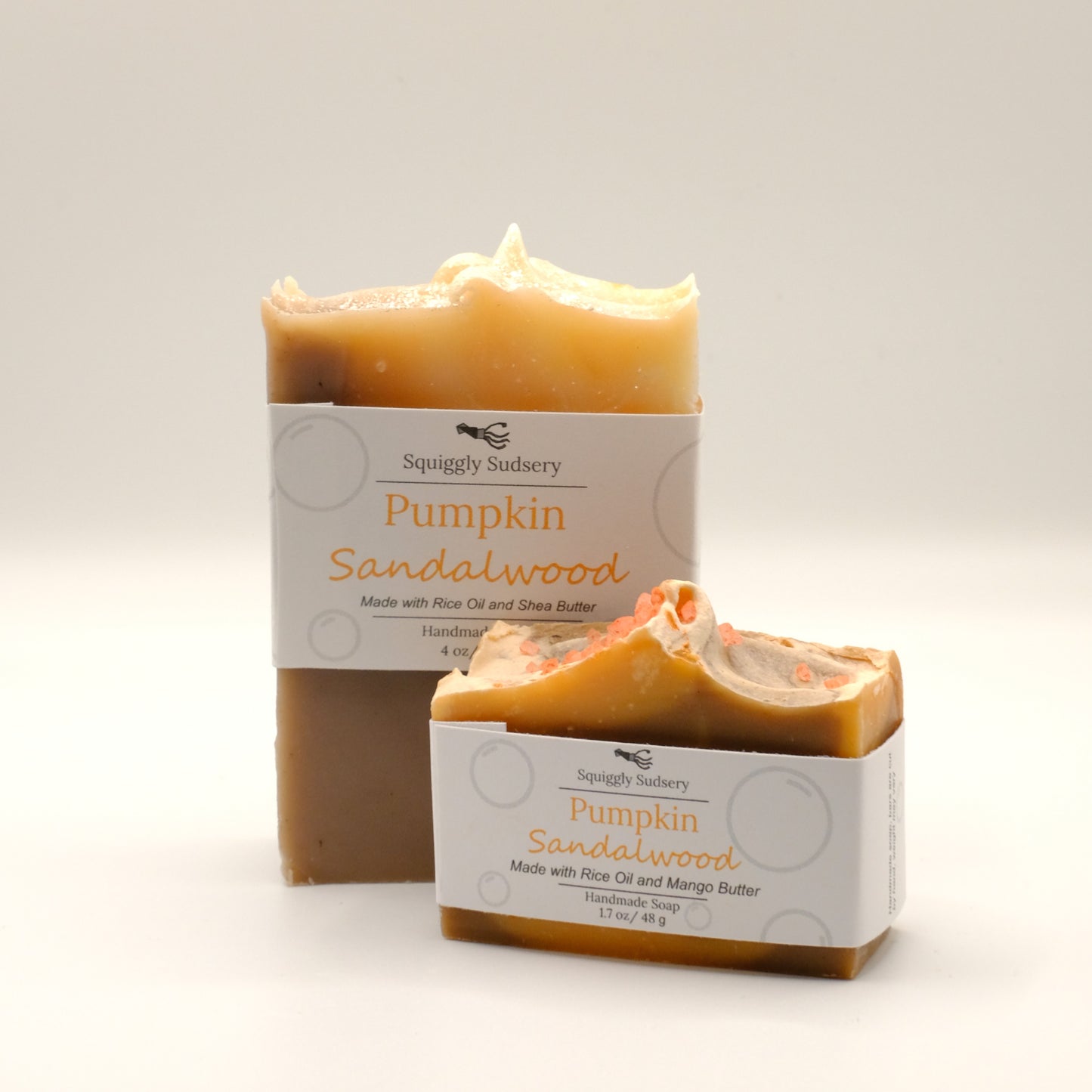 Two brown and orange bars of 'Pumpkin Sandalwood' soap from Squiggly Sudsery on a light background