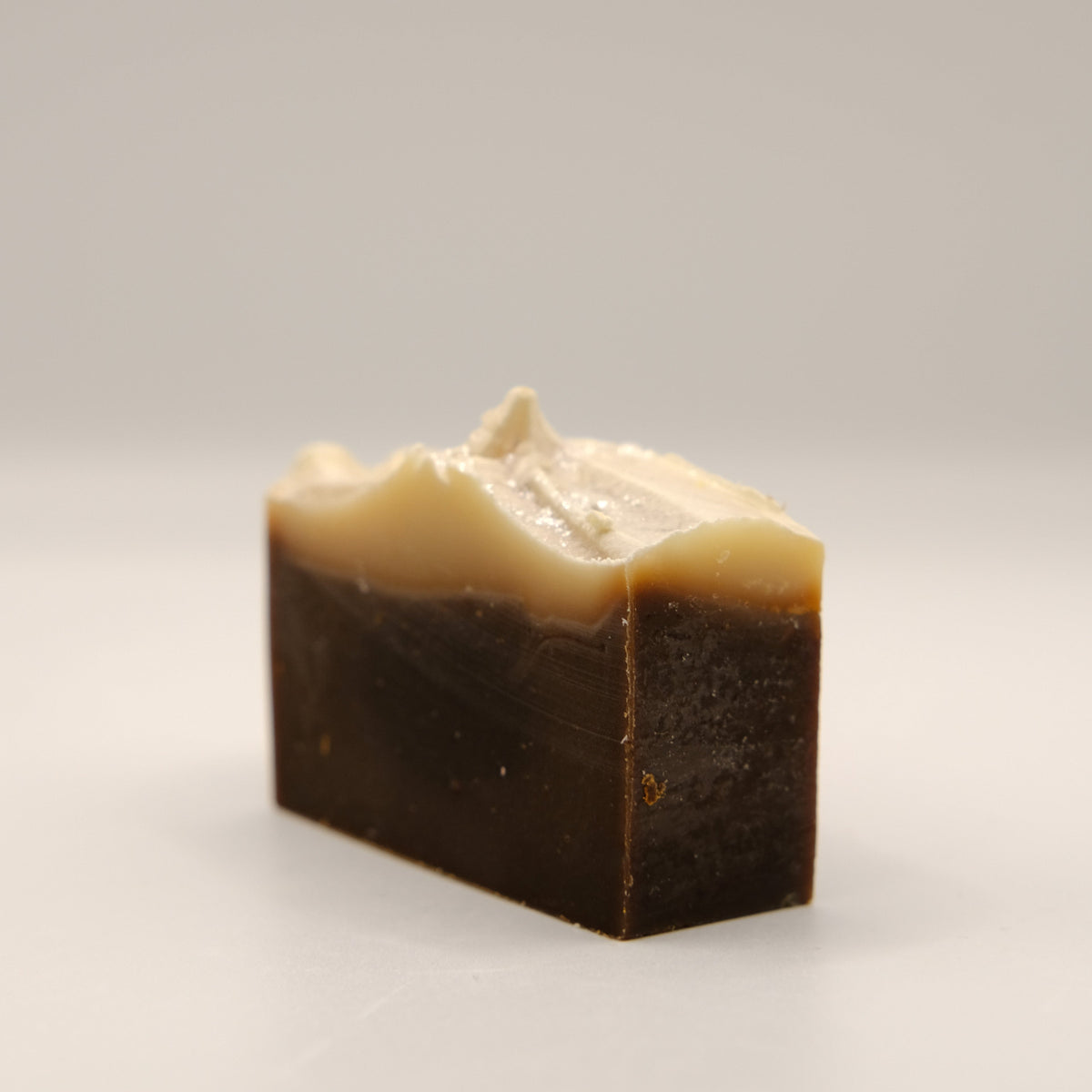 Dark brown soap bar with beige top on a white background