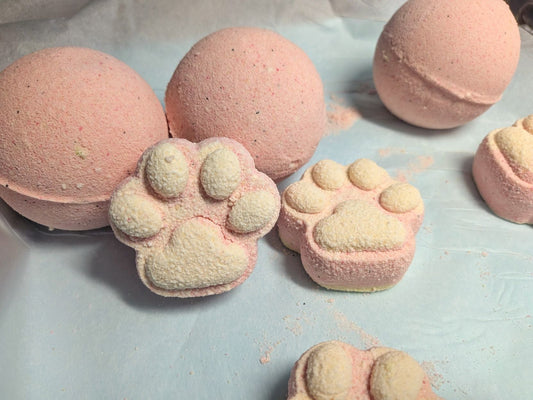Two paw-shaped bath bombs sitting on a tray, with larger, round bath bombs behind them