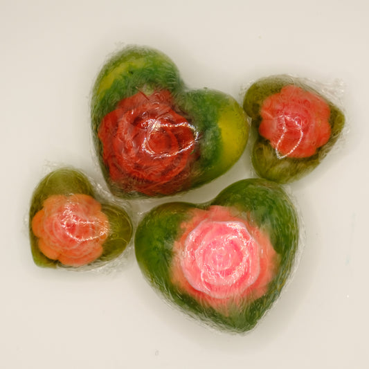 Four green and red heart-shaped soaps with flower embeds on a white background