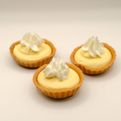 Three small lemon tart-shaped soap with whipped cream on a beige background