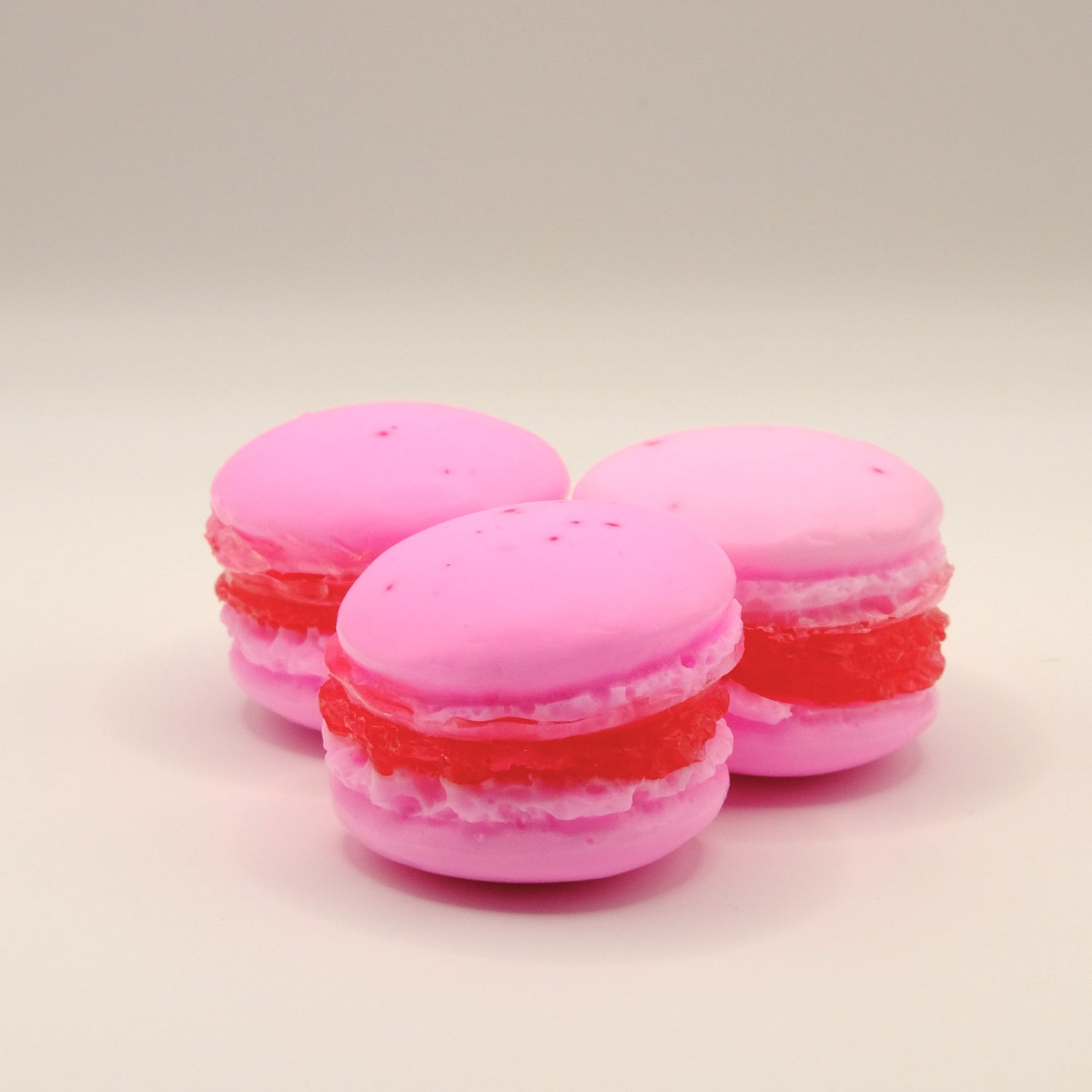 Three pink macaron-shaped soaps with red filling on a beige background