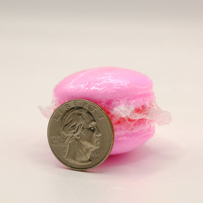 Pink macaron-shaped soap bar in clear packaging next to a U.S. quarter on a light background