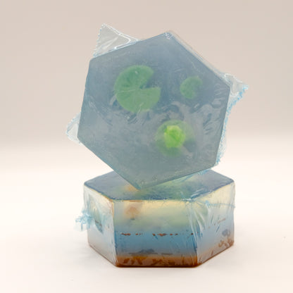 Two hexagonal soap bars with mini frogs and lily pad design on a light gray background