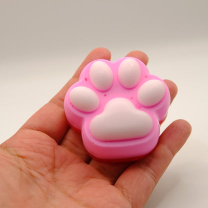 Pink and white paw-shaped soap bar held in a hand against a plain background