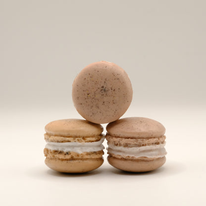 Three brown macaron-shaped soap with white filling stacked on a beige background