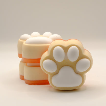 Three yellow, orange and white soap bars with a paw print design on a light gray background