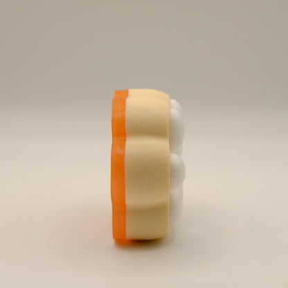 Yellow, orange and white soap bar with a paw print design on a light gray background