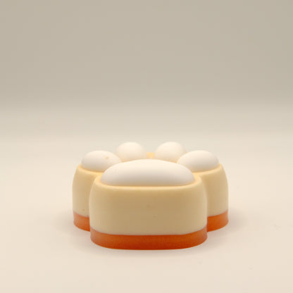 Yellow, orange and white soap bar with a paw print design on a light gray background