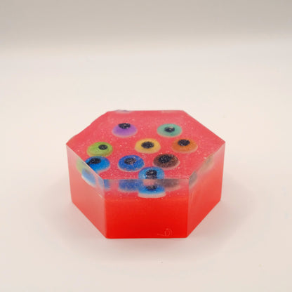 Hexagonal red soap bar with colorful eye-shaped designs on a beige background