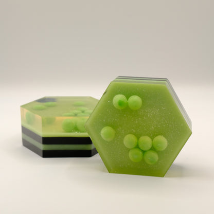 Hexagonal green and black striped soap with embedded spheres on a light gray background