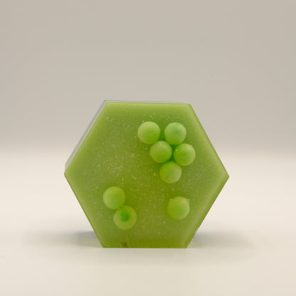 Hexagonal green soap bar with embedded spheres on a beige background