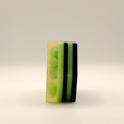 Hexagonal soap bar with green and black stripes and green spheres embedded on a beige background