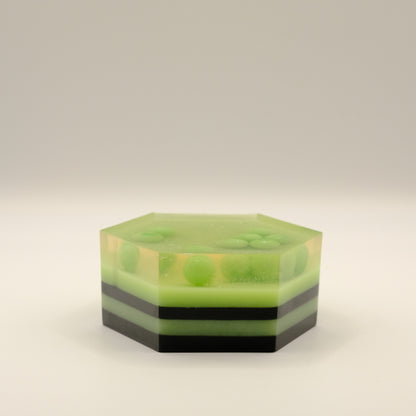 Hexagonal green and black striped soap with embedded spheres on a light gray background