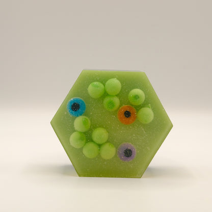 Hexagonal green soap bar embedded with green spheres and eye-shaped designs on a light gray background
