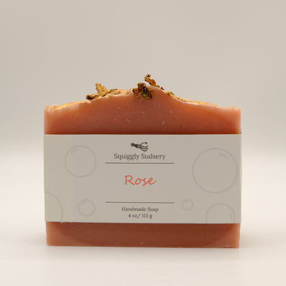 Handmade soap bar with 'Rose' scent from Squiggly Sudsery and a textured top with gold accents on a light background