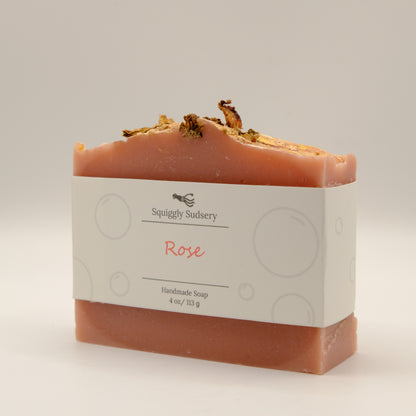 Handmade soap bar with 'Squiggly Sudsery' branding and a textured top with gold accents on a light background