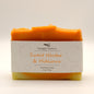 Orange and yellow bar of soap with 'Squiggly Sudsery' branding and 'Sweet Nectar & Hibiscus' description on a light background