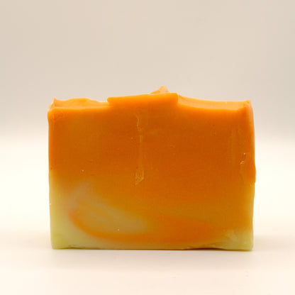Bar of soap with orange and yellow swirls and a textured top on a beige background