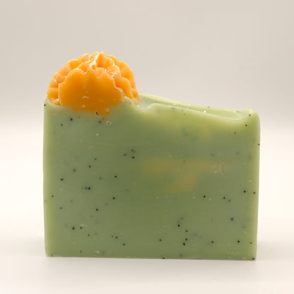 Green soap bar with orange flower and specks on a white background
