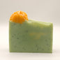 Green soap bar with orange flower and specks on a white background