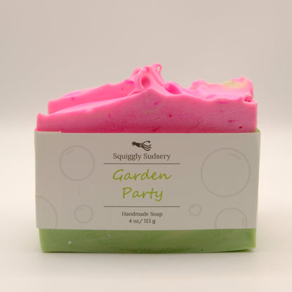Handmade soap bar with pink top and green bottom on a white background, branded 'Squiggly Sudsery'.