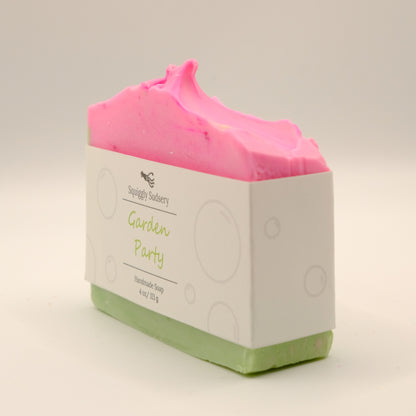 Bar of soap with pink top and green bottom with white packaging labeled 'Garden Party' on a light gray background
