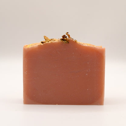 Pink bar of soap with natural elements and gold accents on a white background