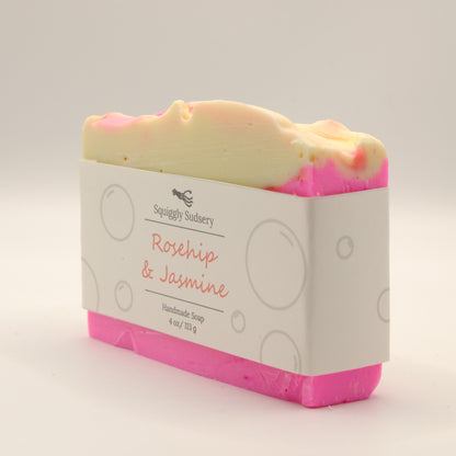 Bar of soap with pink and beige layers on a white background, featuring 'Squiggly Sudsery' branding.