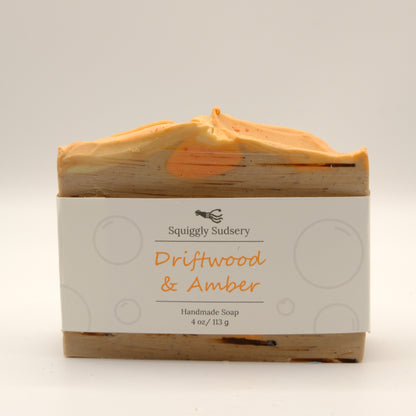 Bar of soap with 'Squiggly Sudsery' branding and 'Driftwood & Amber' scent on a white background