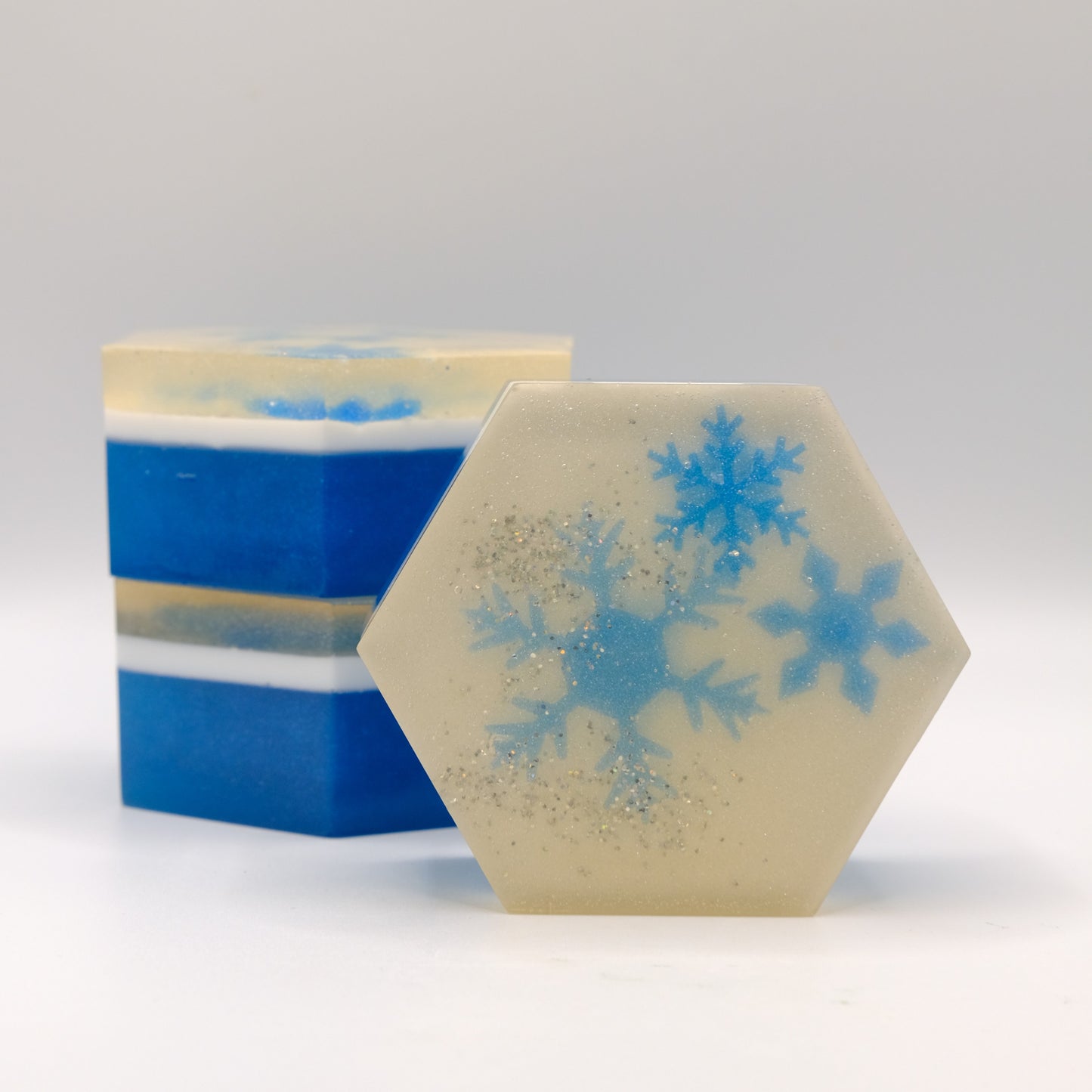 Three blue and white hexagonal soap bars with blue snowflake designs on a gray background