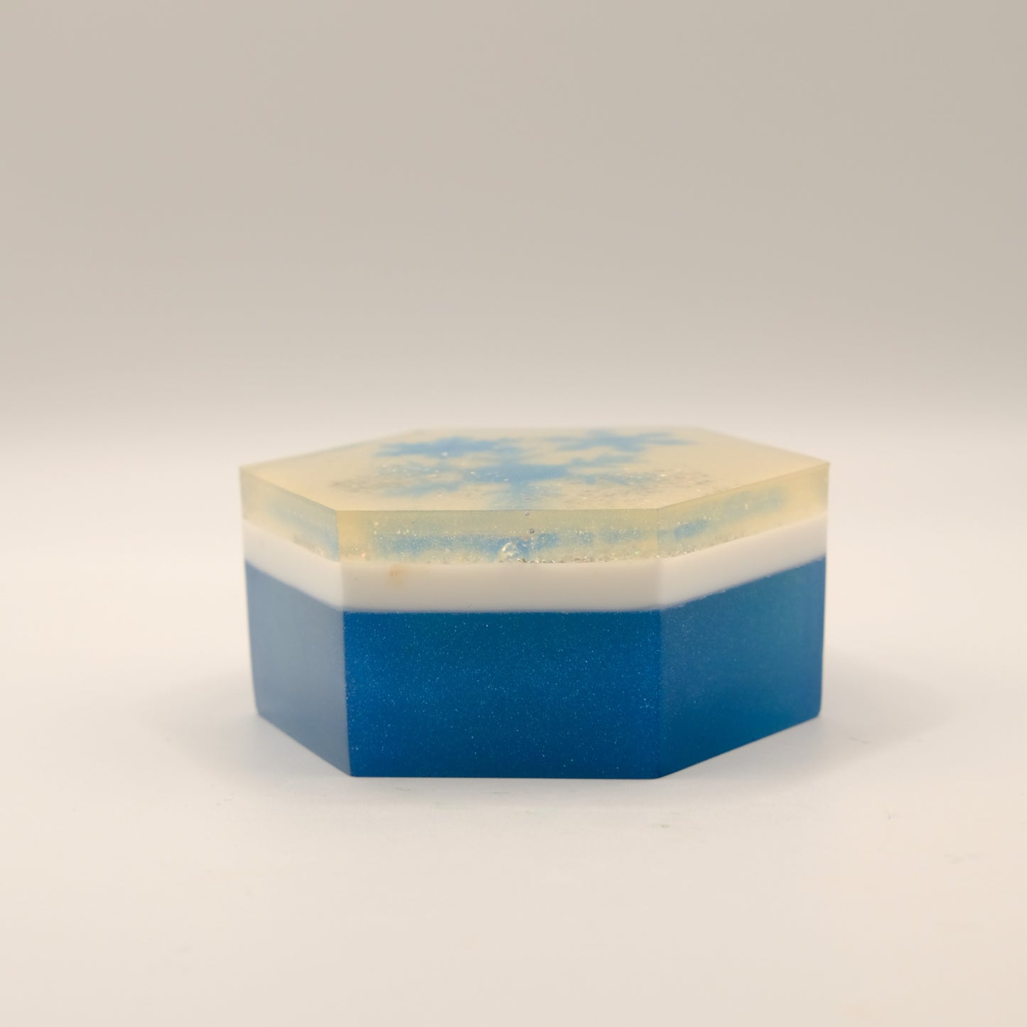 Hexagonal soap bar with blue and white layers on a light gray background