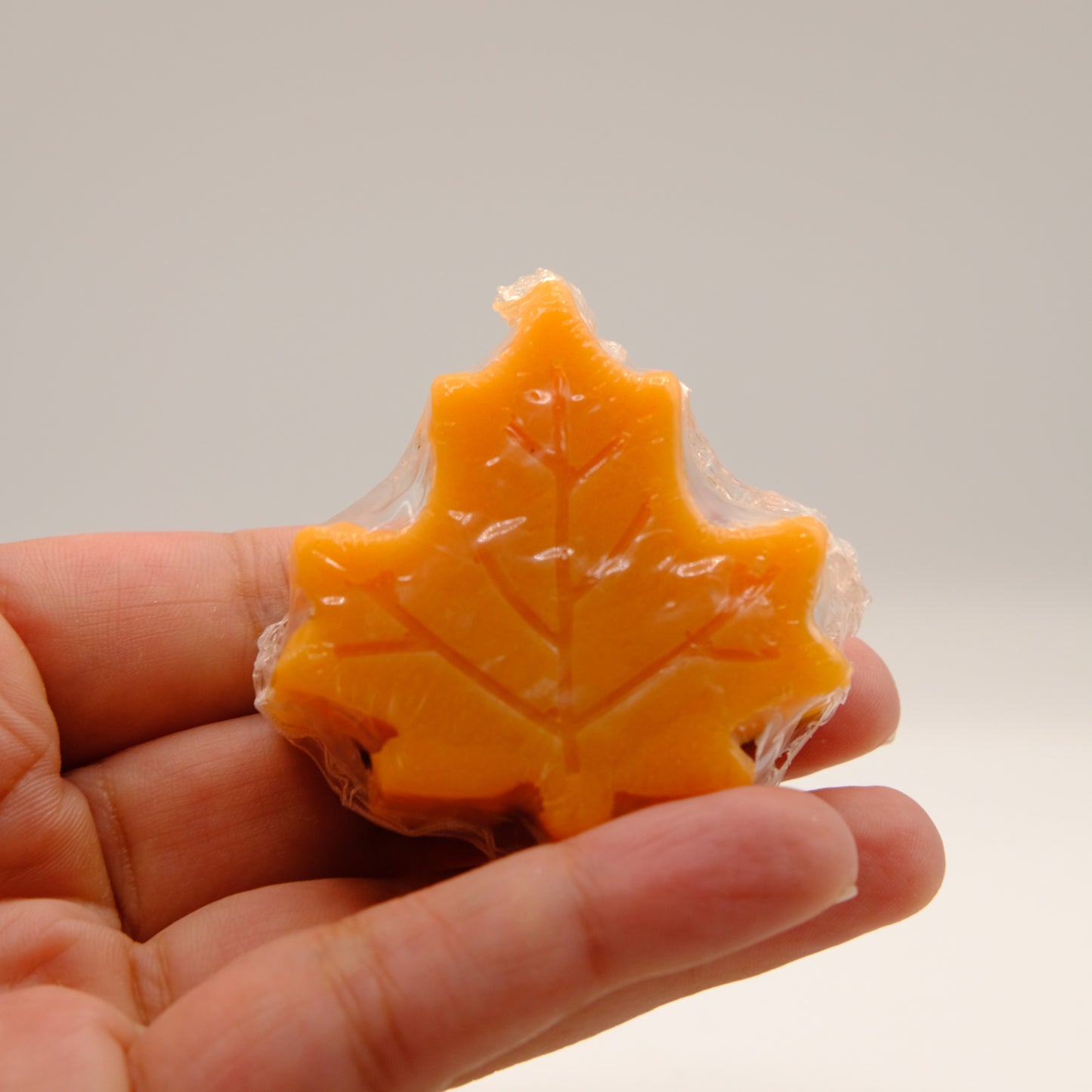 Maple leaf-shaped soap held in a hand against a neutral background