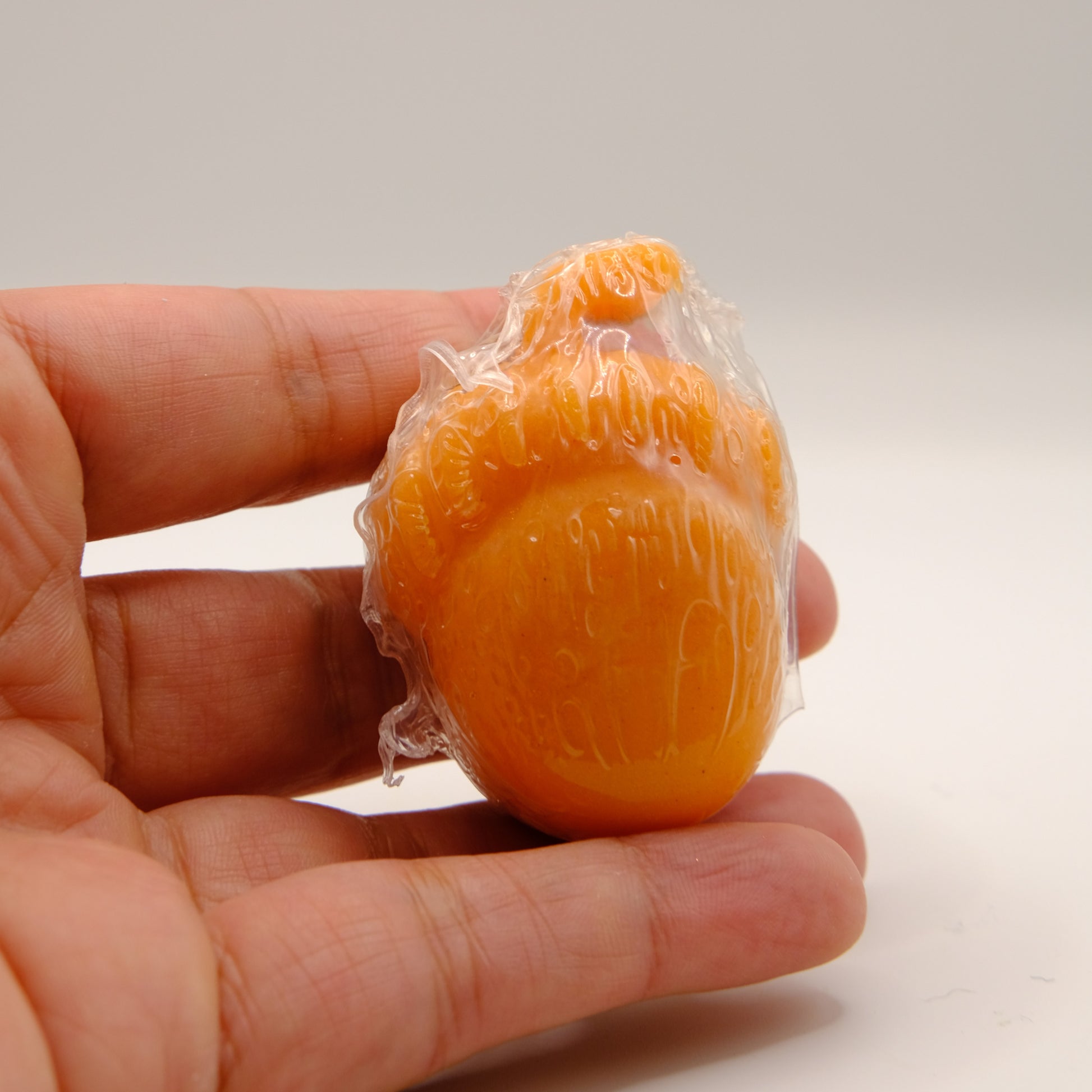 Orange acorn-shaped soap bar with plastic wrap held in a hand against a plain background