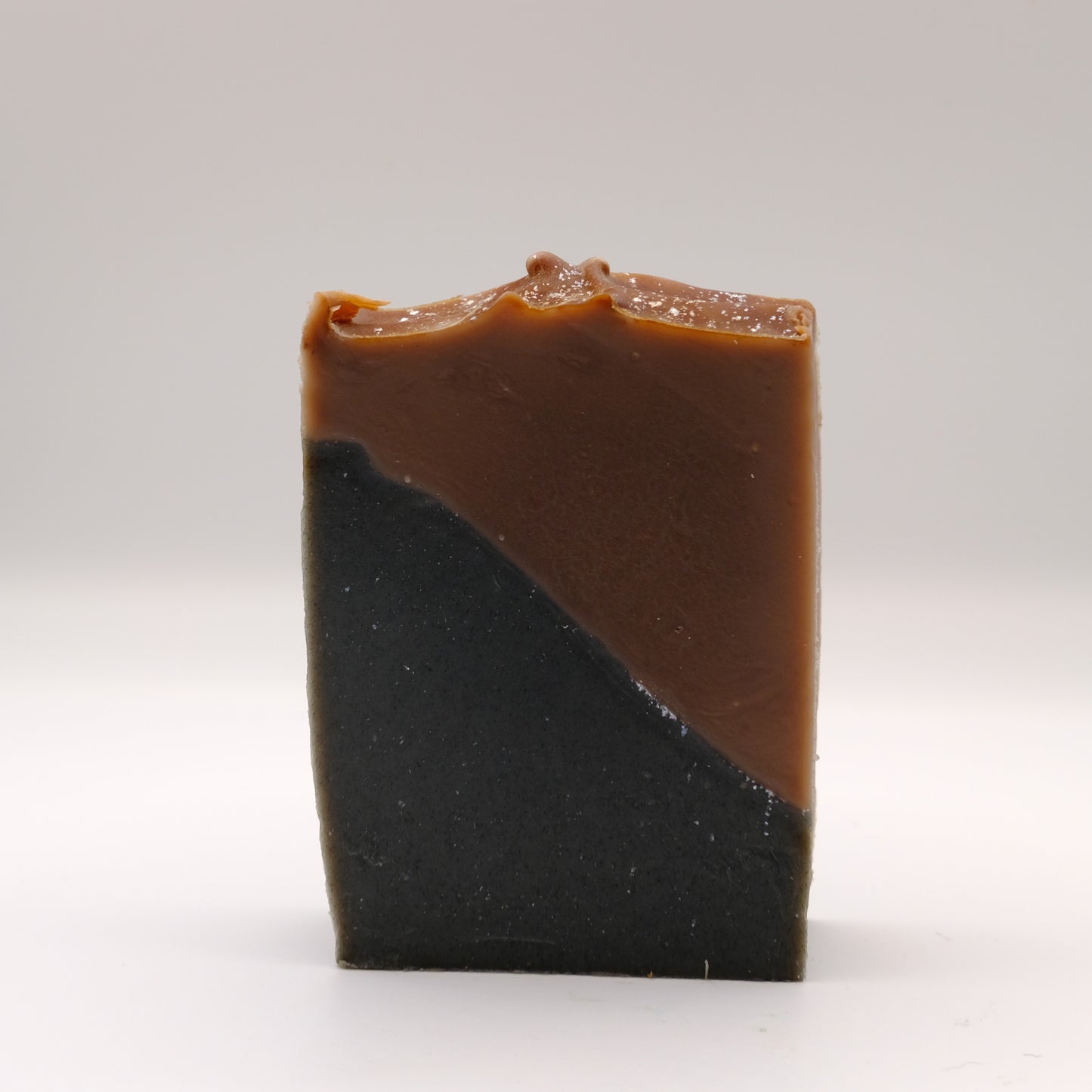 Two-toned brown and black soap bar with a textured top and silver accents on a white background