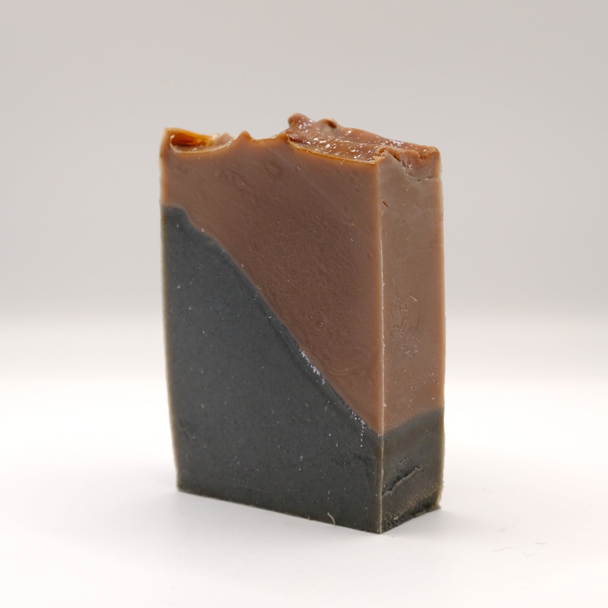 Two-tone brown and black soap bar with a textured top and silver accents on a white background