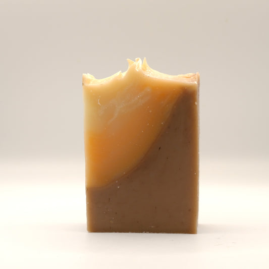 Bar of soap with a textured top and a gradient from beige to orange to dark brown on a white background