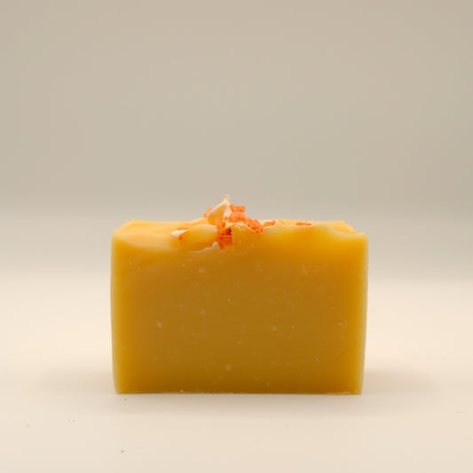 Yellow bar of soap with orange specks and textured top on a beige background