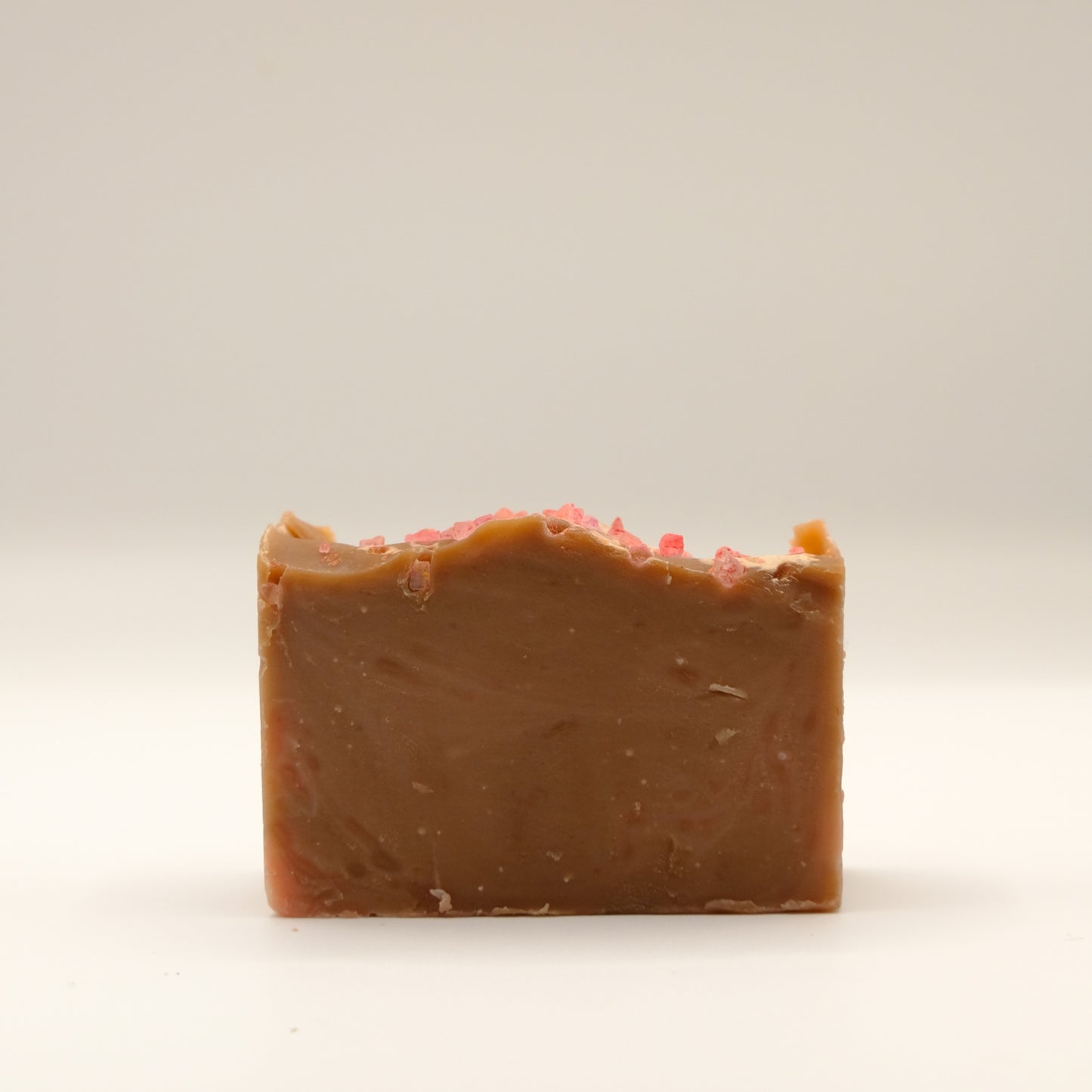 Bar of brown soap with pink specks on a light beige background