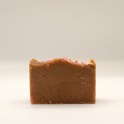 Bar of brown soap with pink specks on a light beige background