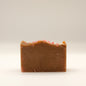 Bar of brown soap with pink specks on a light beige background