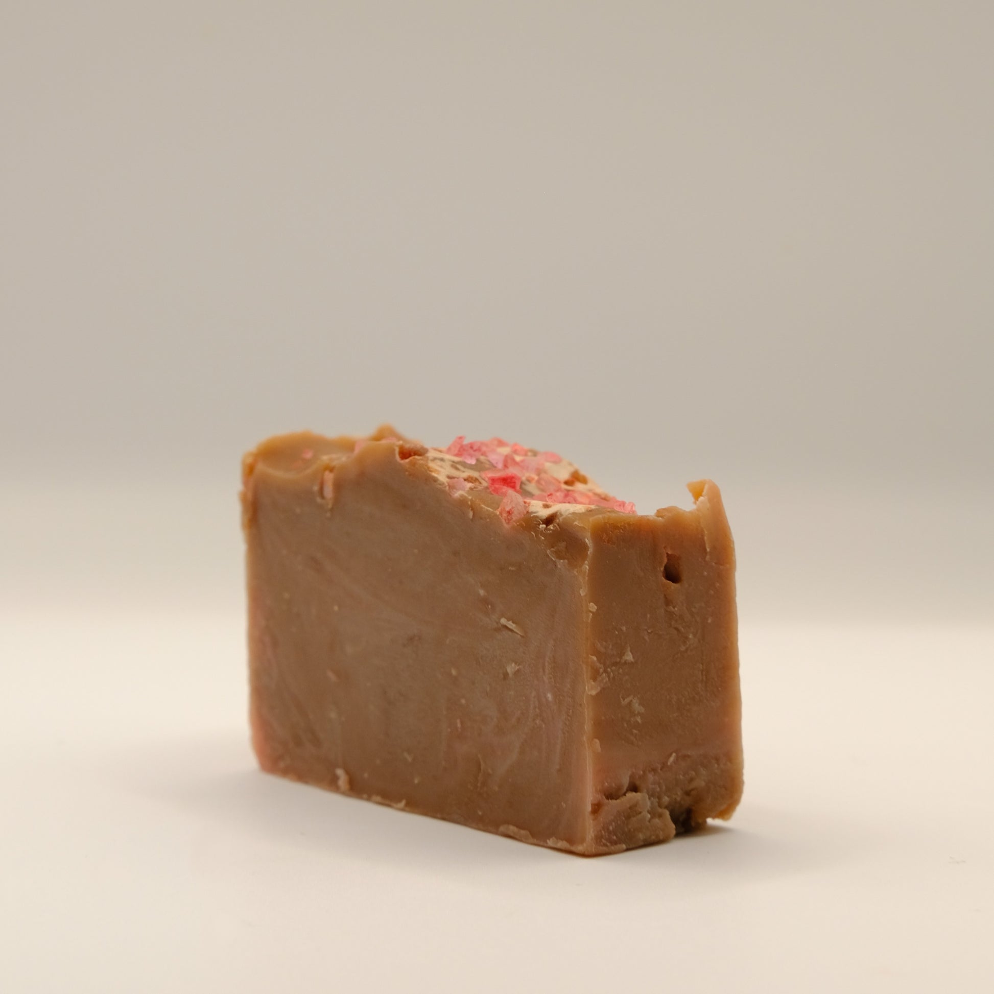 Bar of brown soap with pink speckles on a beige background