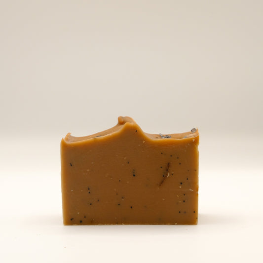 Brown bar of soap with specks and a textured top on a beige background