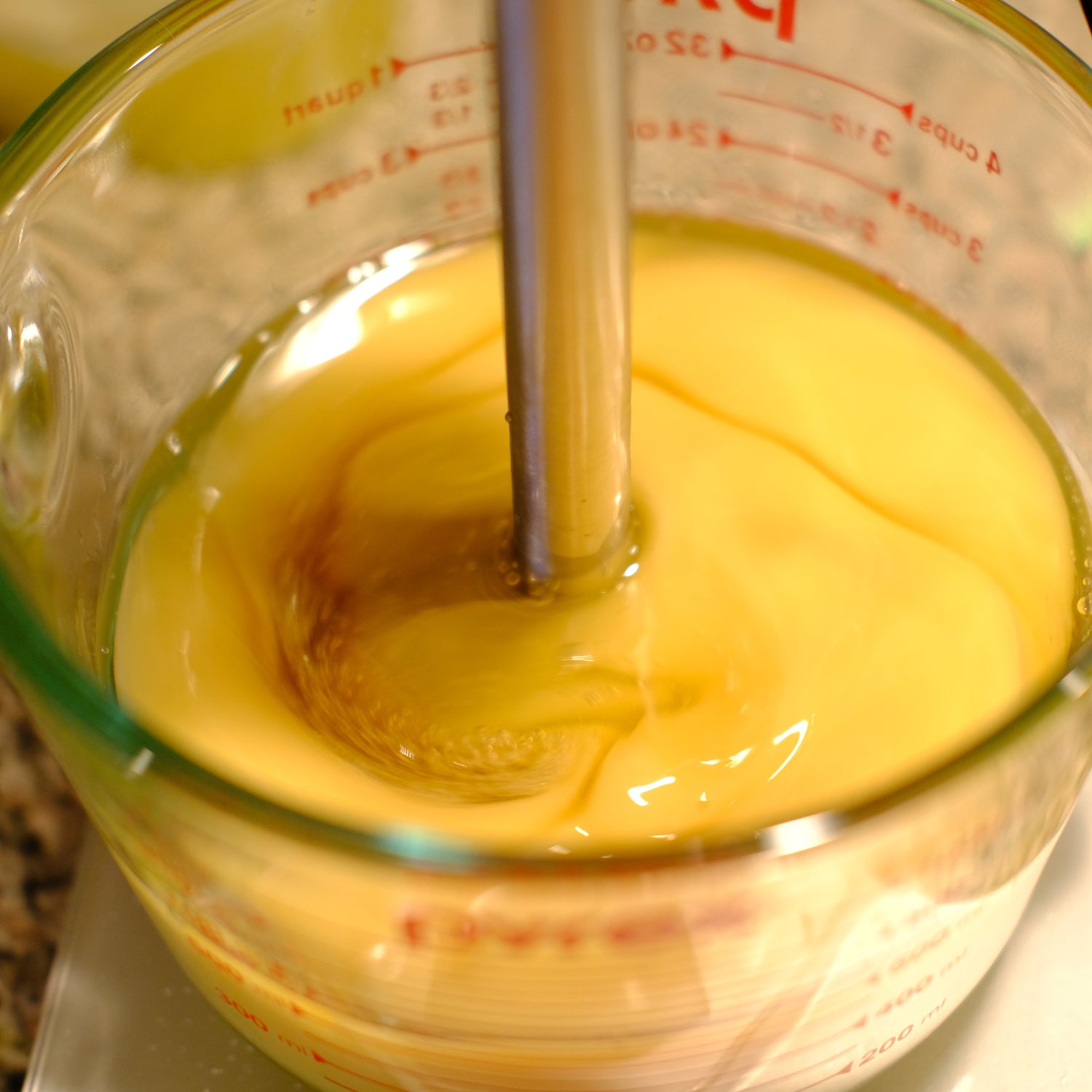 Yellow liquid being mixed in a glass measuring cup with an immersion blender.