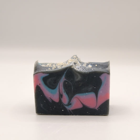 Bar of soap with black, pink, purple, and blue swirls on a white background