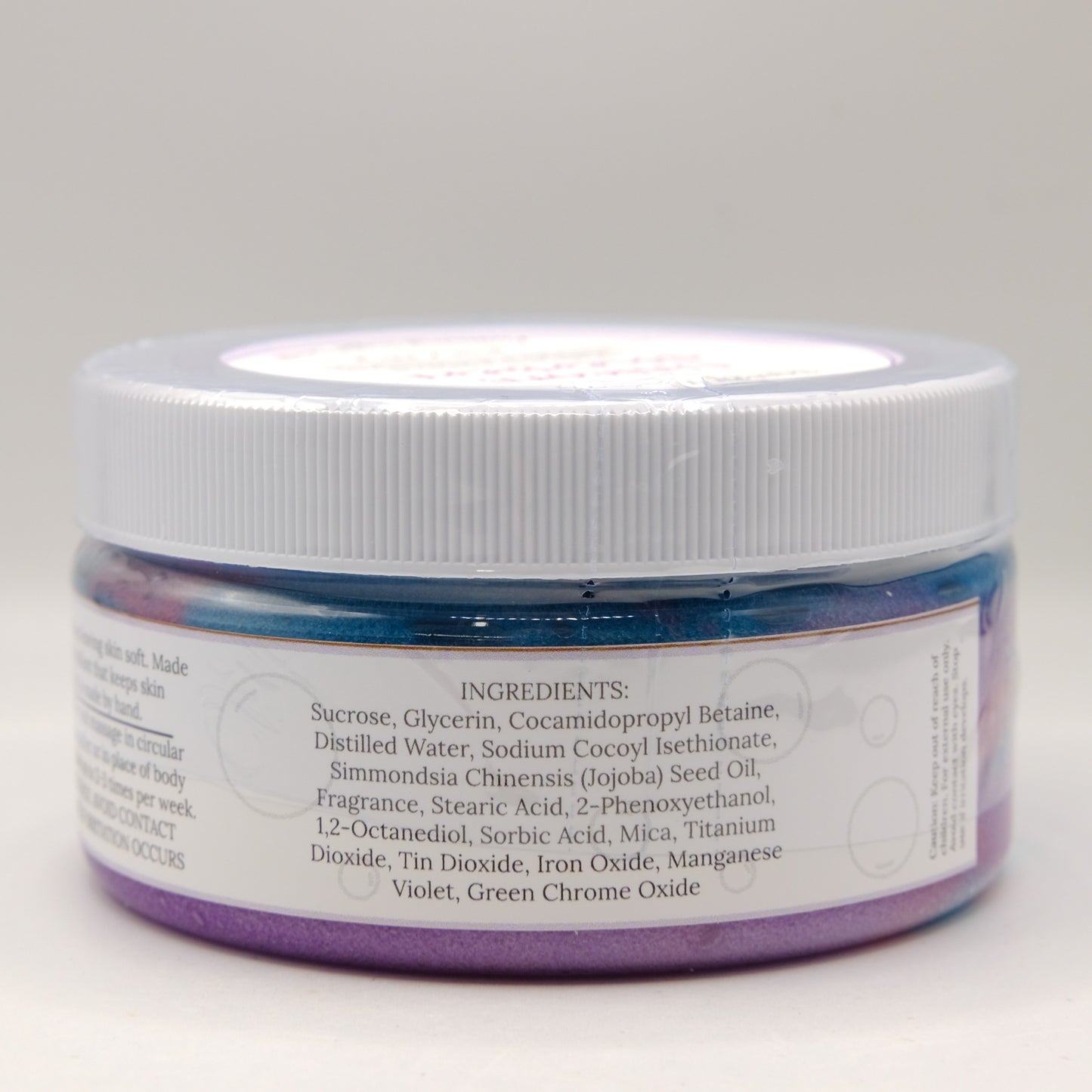 Jar of purple and blue sugar scrub with a white lid on a light gray background