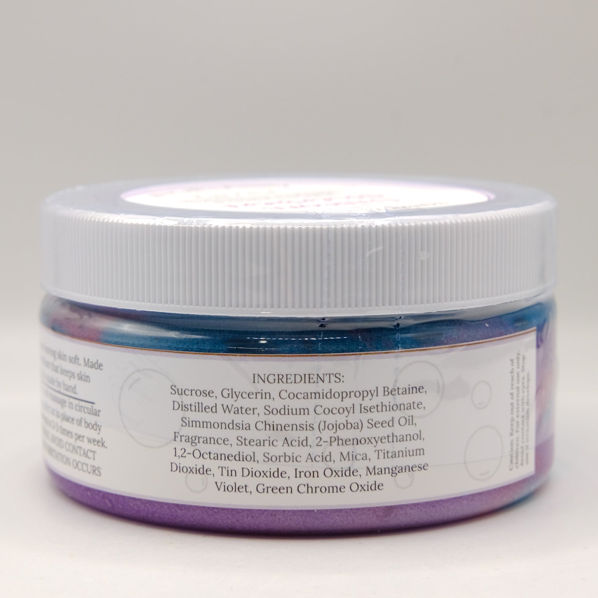 Jar of purple and blue sugar scrub with a white lid on a light gray background
