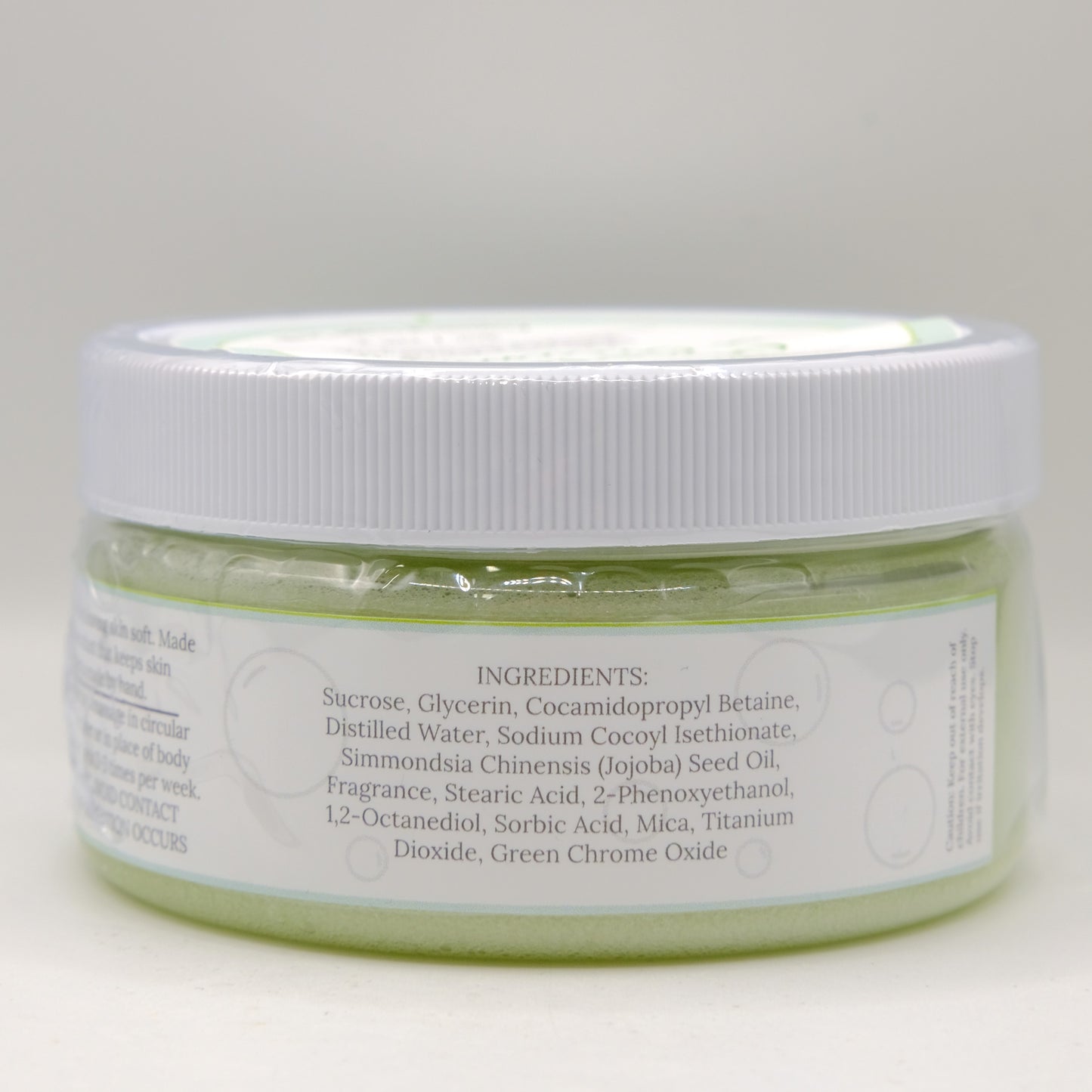 Jar of green sugar scrub with white lid on a light gray background